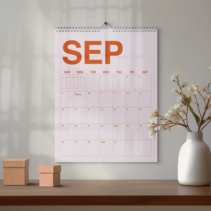May include: A wall calendar for the month of September featuring large orange text reading SEP at the top. The grid displays days of the week from Sunday to Saturday with numbered dates in a light orange color, suspended by a silver metal wire coil.