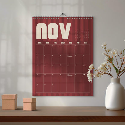 May include: A wall calendar for the month of November featuring a deep red background with vertical stripes, white text, and a grid layout. The calendar displays the days of the week and dates, with Veterans Day and Thanksgiving marked on the grid.