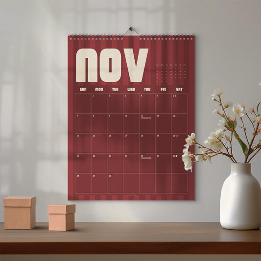 May include: A wall calendar for the month of November featuring a deep red background with vertical stripes, white text, and a grid layout. The calendar displays the days of the week and dates, with Veterans Day and Thanksgiving marked on the grid.