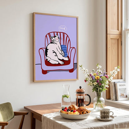 May include: A framed art print featuring a relaxed cat sitting in a red armchair against a lavender background. The cat is white with black markings. A thought bubble with a fishbone is above the cat's head. The print is in a light wood frame.