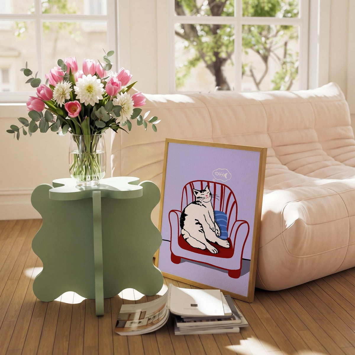 May include: A framed cat art print featuring a black and white cat lounging in a red armchair. A bouquet of pink tulips and white dahlias sits in a clear vase on a light green side table. A stack of books rests on the floor.