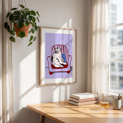 May include: A framed art print featuring a white and black cat sitting in a red armchair with a blue pillow. The background is a light purple color. The print is displayed on a wall near a window and a wooden desk.