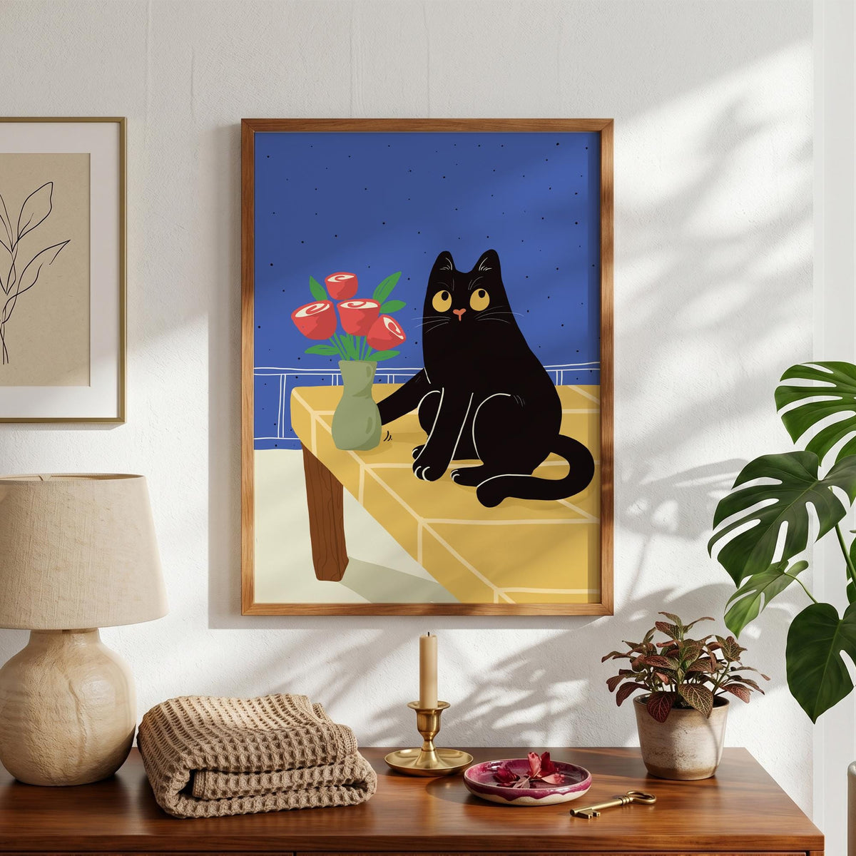 May include: A framed art print featuring a black cat with yellow eyes sitting on a yellow table. A vase of red roses sits next to the cat. The background is blue, and the frame is brown.