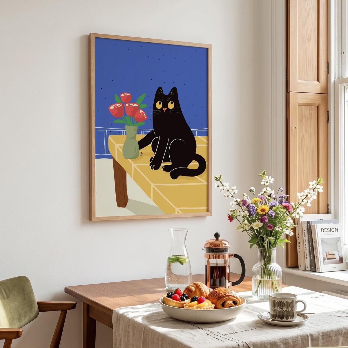 May include: A framed art print featuring a black cat sitting on a yellow table with a vase of red roses. The background is a blue night sky. The print is displayed in a room with a table set for breakfast.