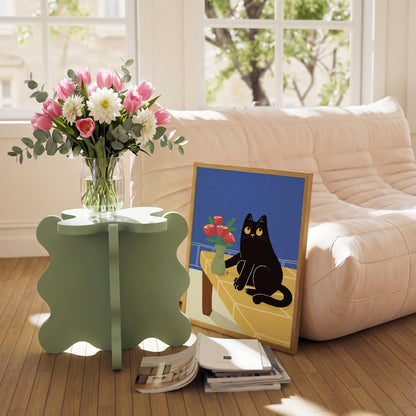May include: A light green, four-leaf clover-shaped side table holds a clear glass vase filled with pink tulips, white dahlias, and eucalyptus. A framed art print of a black cat and a vase of red roses rests on the floor.
