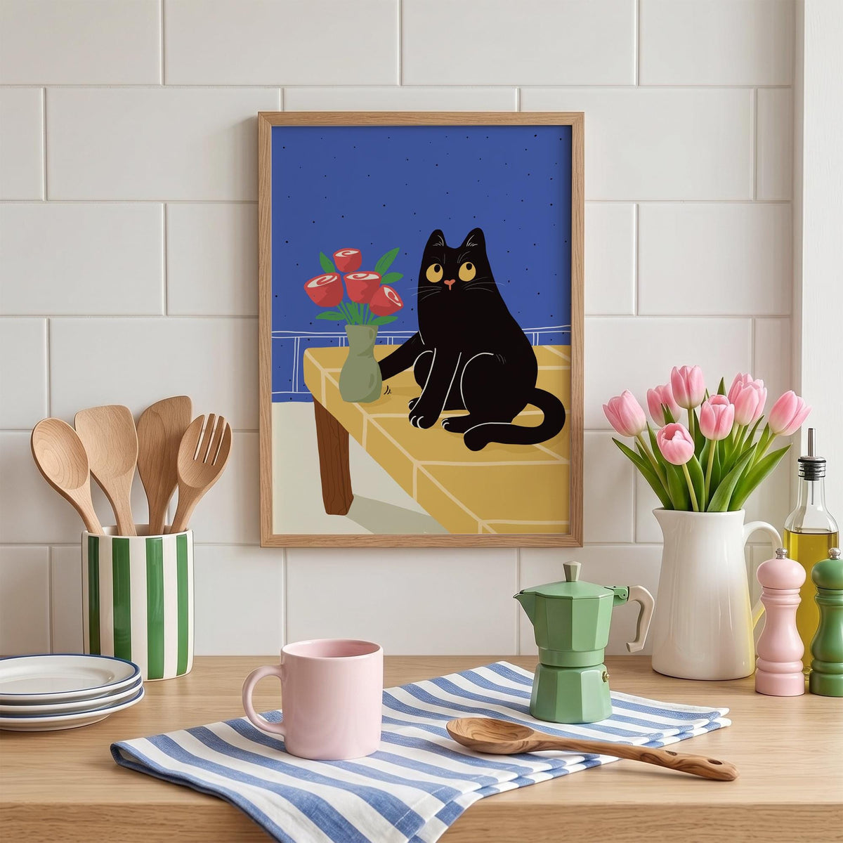 May include: A framed art print depicts a black cat sitting on a yellow table with a vase of red roses. The cat has yellow eyes and is set against a blue background. Kitchen utensils, a pink mug, and a green coffee maker are also visible.