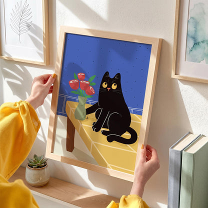 May include: A framed art print featuring a black cat sitting on a yellow table with a vase of red roses. The background is blue. The print is in a light wood frame.