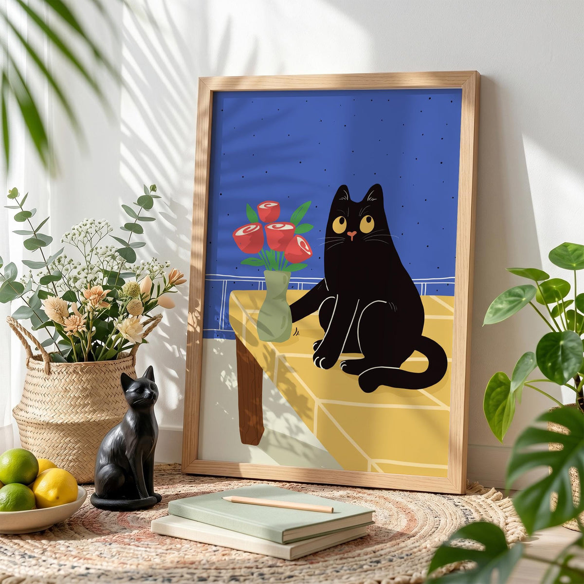 May include: A framed art print featuring a black cat sitting on a yellow table with a vase of red roses. The background is blue. A black cat figurine and a basket of flowers are in the foreground.